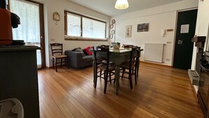 Una habitación con mesa de comedor, sillas, sofá, ventana con cortinas, radiador y puerta.