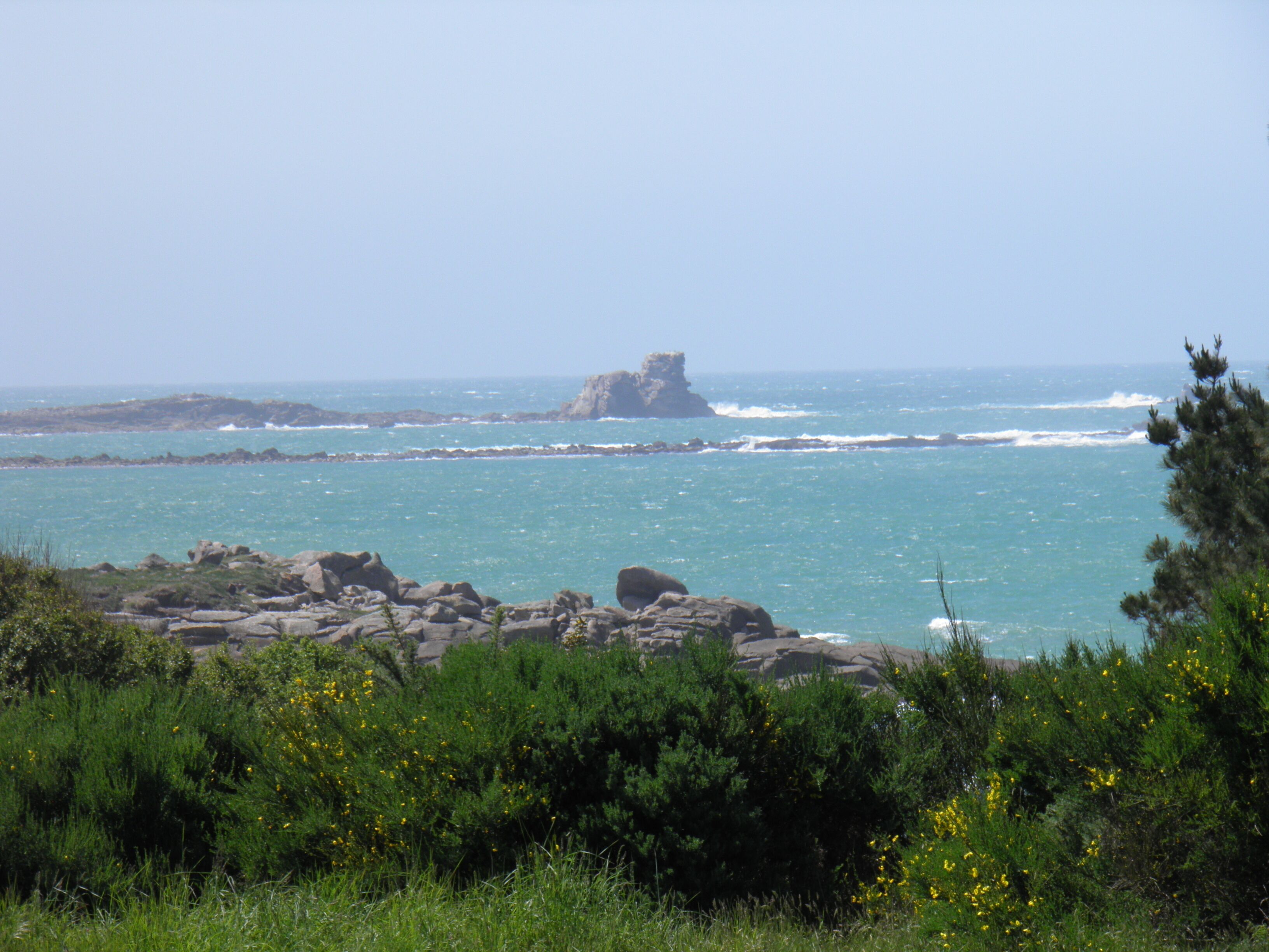 A coastal landscape with rocky terrain, greenery, and a clear view of the sea.
