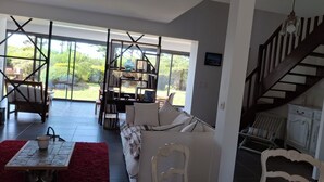 A spacious living area with a large window, a staircase, and a bookshelf. - Landrellec plage, large 4-bedroom house, sea view, piano, quiet location. (Pleumeur Bodou)