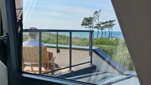 A room with a large window overlooking a balcony with a view of the sea and trees. - Landrellec plage, large 4-bedroom house, sea view, piano, quiet location. (Pleumeur Bodou)