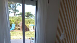 A bedroom with a bed, a nightstand, a lamp, a sliding glass door to a balcony, and a striped wall. - Landrellec plage, large 4-bedroom house, sea view, piano, quiet location. (Pleumeur Bodou)