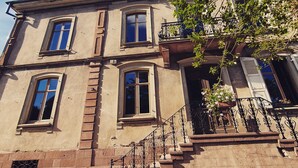 Un bâtiment à deux étages, doté d’une façade en pierre, de nombreuses fenêtres et d’un escalier orné de rampes en fer forgé.