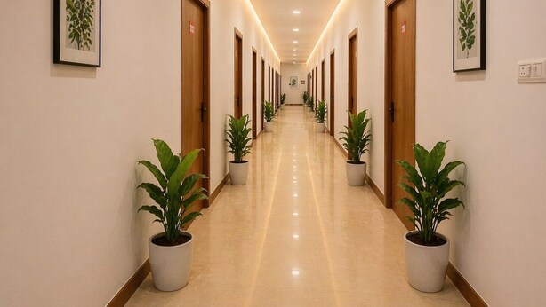 A long, well-lit hallway with wooden doors, potted plants, and framed artwork on the walls. - Mauryan Express Hotel Nangloi Metro (New Delhi)