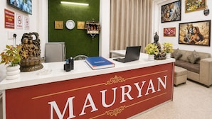 Ein Hotelrezeptionstresen mit einem roten Schild mit der Aufschrift 'MAURYAN', einer Uhr, einer Überwachungskamera und einem Computer.