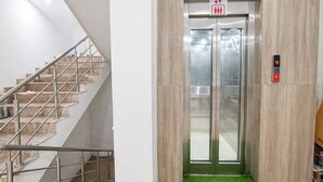 A staircase with metal railings and a wall-mounted elevator with a digital display. - Mauryan Express Hotel Nangloi Metro (New Delhi)