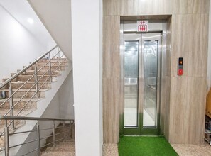 Uma escadaria com corrimãos de metal e um elevador de parede com visor digital.