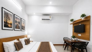 Ein Hotelzimmer mit Bett, Nachttisch, Lampe, Schreibtisch, Stuhl, Fernseher und Wandklimaanlage.