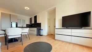 Una sala de estar moderna con una mesa redonda, un sofá, un televisor y una cocina al fondo.