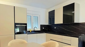 Una cocina moderna con encimera de mármol negro, armarios blancos y una zona de comedor con una mesa y sillas color beige.