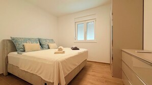 Un dormitorio con cama, almohadas, mesita de noche, ventana y armario.