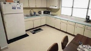 Cocina compacta con armarios blancos, refrigerador, microondas y ventana que proporciona luz natural.