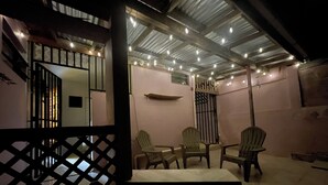 Un patio al aire libre con mesa y sillas, techo de metal y luces colgantes.