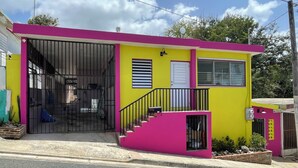 Un edificio pequeño y colorido, con entrada visible, una escalera y un área exterior cercada.