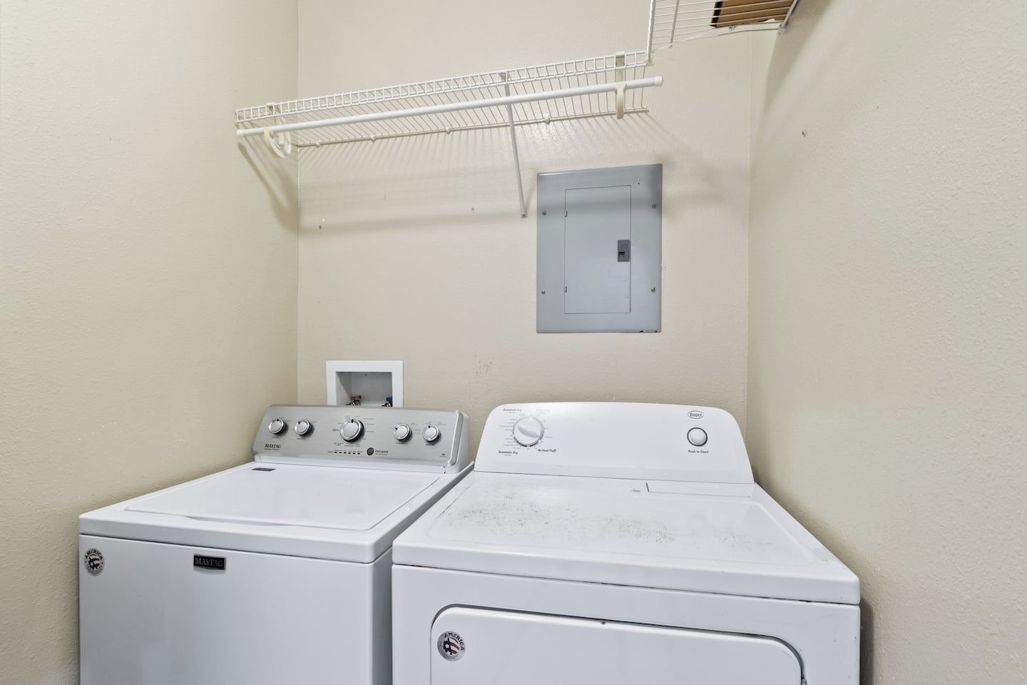 A laundry room with two stacked washers and dryers, a metal drying rack, and a wall-mounted electrical box.