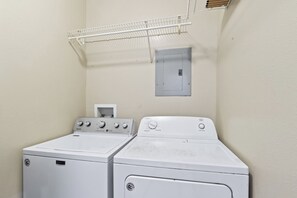 A laundry room with two stacked washers and dryers, a metal drying rack, and a wall-mounted electrical box. - Coastal Lower Unit: Beach Access & Fire Pit (Gulf Shores)