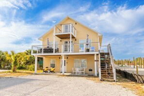 Una casa davant del mar de dos pisos amb un balcó, mobiliari exterior i una escala que condueix al pis superior.