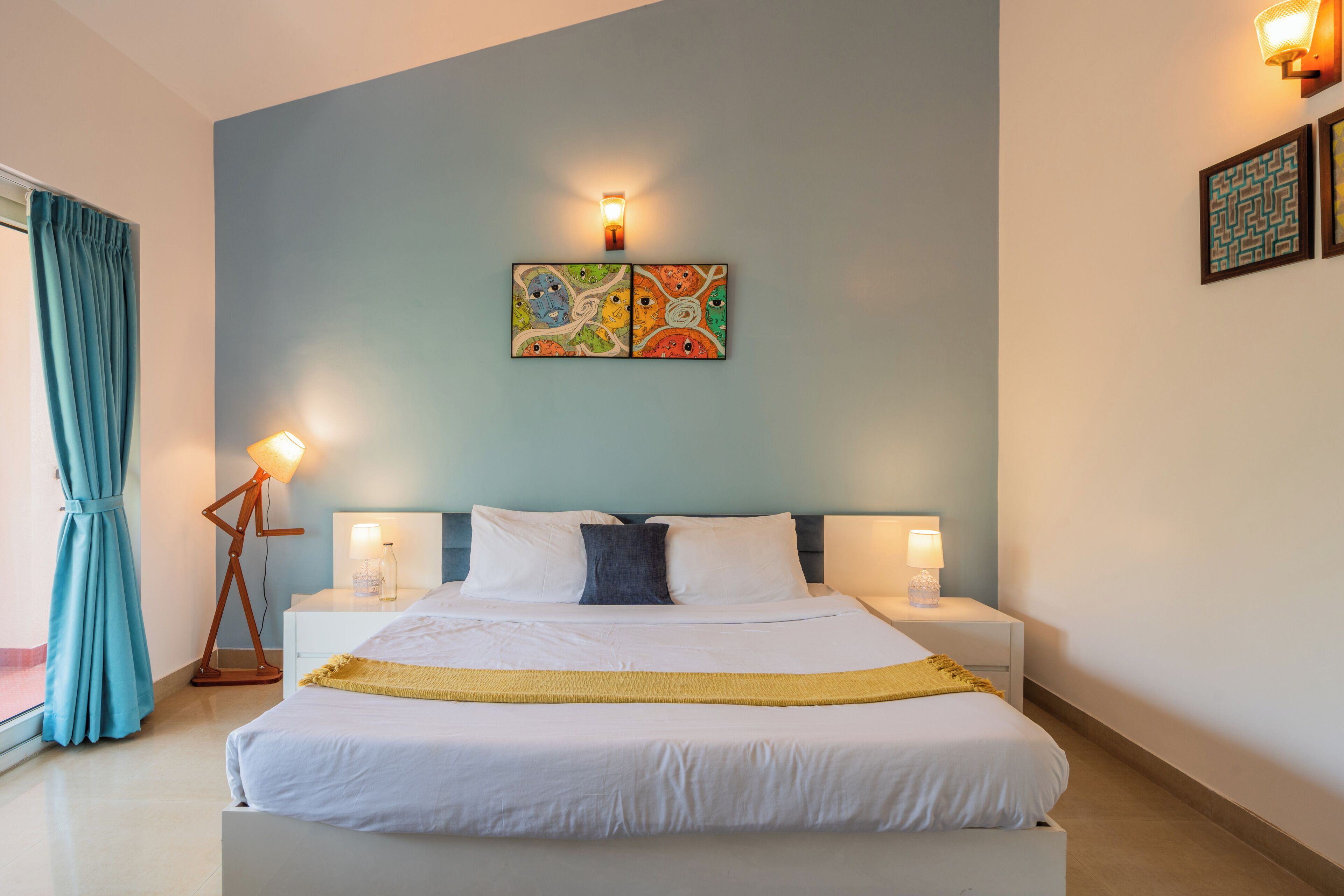 A hotel room with a bed, bedside lamps, a wall-mounted artwork, and a window with curtains.