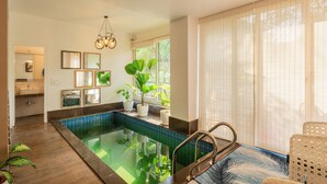 An indoor swimming pool with a tiled edge, a ceiling light fixture, and potted plants. - Alaya Stays 3 BHK Casa Bella Vista  (Nerul)