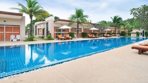 A swimming pool with lounge chairs and umbrellas, surrounded by palm trees and buildings. - Blue Palm Seafront Resort Phuket (Rawai)