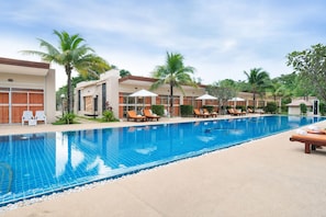 A swimming pool with lounge chairs and umbrellas, surrounded by palm trees and buildings. - Blue Palm Seafront Resort Phuket (Rawai)