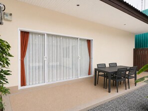 A patio area with a sliding glass door, a table with chairs, and a potted plant. - Blue Palm Seafront Resort Phuket (Rawai)