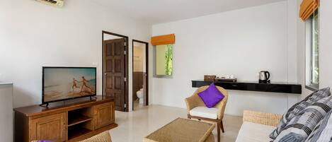 A modern living room with a flat-screen TV, wicker furniture, a coffee table, and a sofa with patterned cushions.