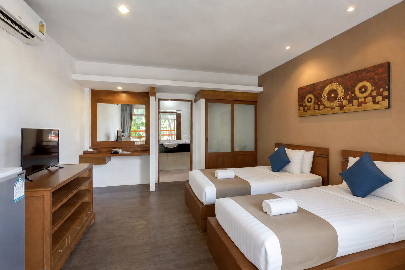 A hotel room with two beds, a TV, a desk, and a bathroom visible through an open door.