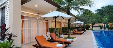 A poolside area with lounge chairs, umbrellas, and a swimming pool.