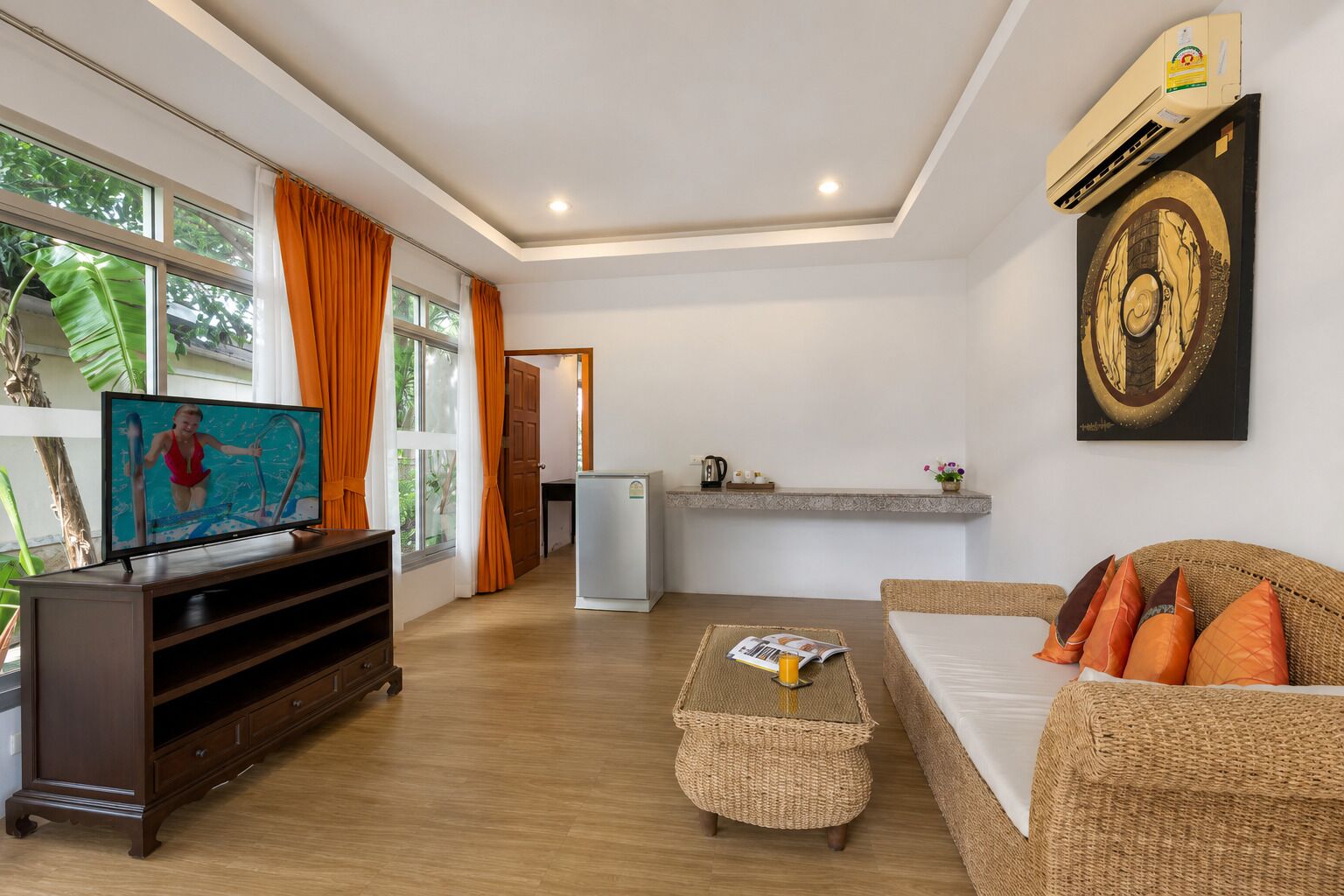 A living room with a television, a sofa, a coffee table, and a kitchen area in the background.