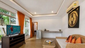A living room with a television, a sofa, a coffee table, and a kitchen area in the background. - Blue Palm Seafront Resort Phuket (Rawai)