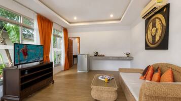 A living room with a television, a sofa, a coffee table, and a kitchen area in the background.