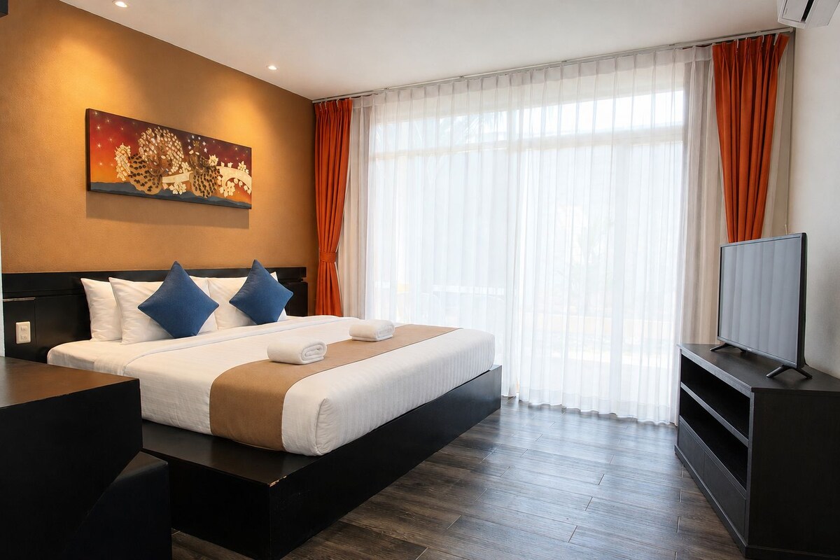 A hotel room with a bed, a flat-screen TV, a painting on the wall, and a large window with curtains.