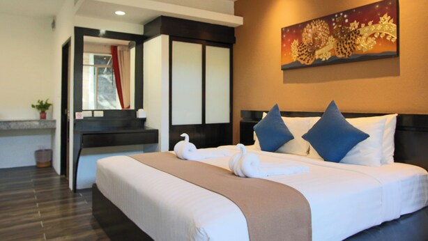 A hotel room with a bed, a nightstand, a painting, and a window with curtains. - Blue Palm Seafront Resort Phuket (Rawai)