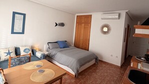 Ein Schlafzimmer mit einem Bett, einem Holzschrank, einem Nachttisch, einer wandmontierten Klimaanlage und einem kleinen Tisch mit Stuhl.