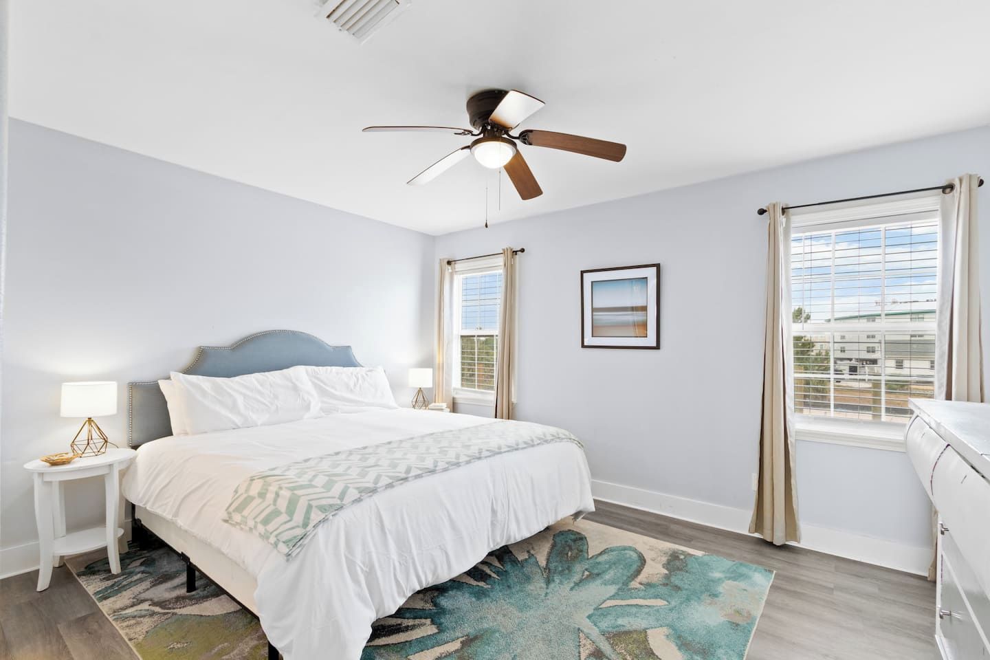 A bedroom with a bed, nightstands, a ceiling fan, a window with curtains, and a view of the outside.