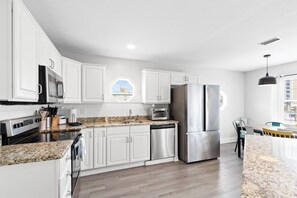 A modern kitchen with white cabinetry, stainless steel appliances, and a granite countertop. - Coastal Upper Unit: Beach Access & Fire Pit (Gulf Shores)