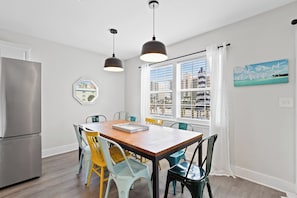 A modern kitchen with a stainless steel refrigerator, a wooden dining table with chairs, and pendant lighting. - Coastal Upper Unit: Beach Access & Fire Pit (Gulf Shores)