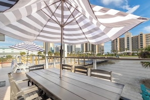 An outdoor seating area with striped umbrellas, wooden tables, and chairs. - Coastal Upper Unit: Beach Access & Fire Pit (Gulf Shores)