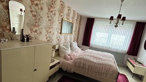 Een slaapkamer met een bed, een kaptafel, een spiegel en een raam met gordijnen.