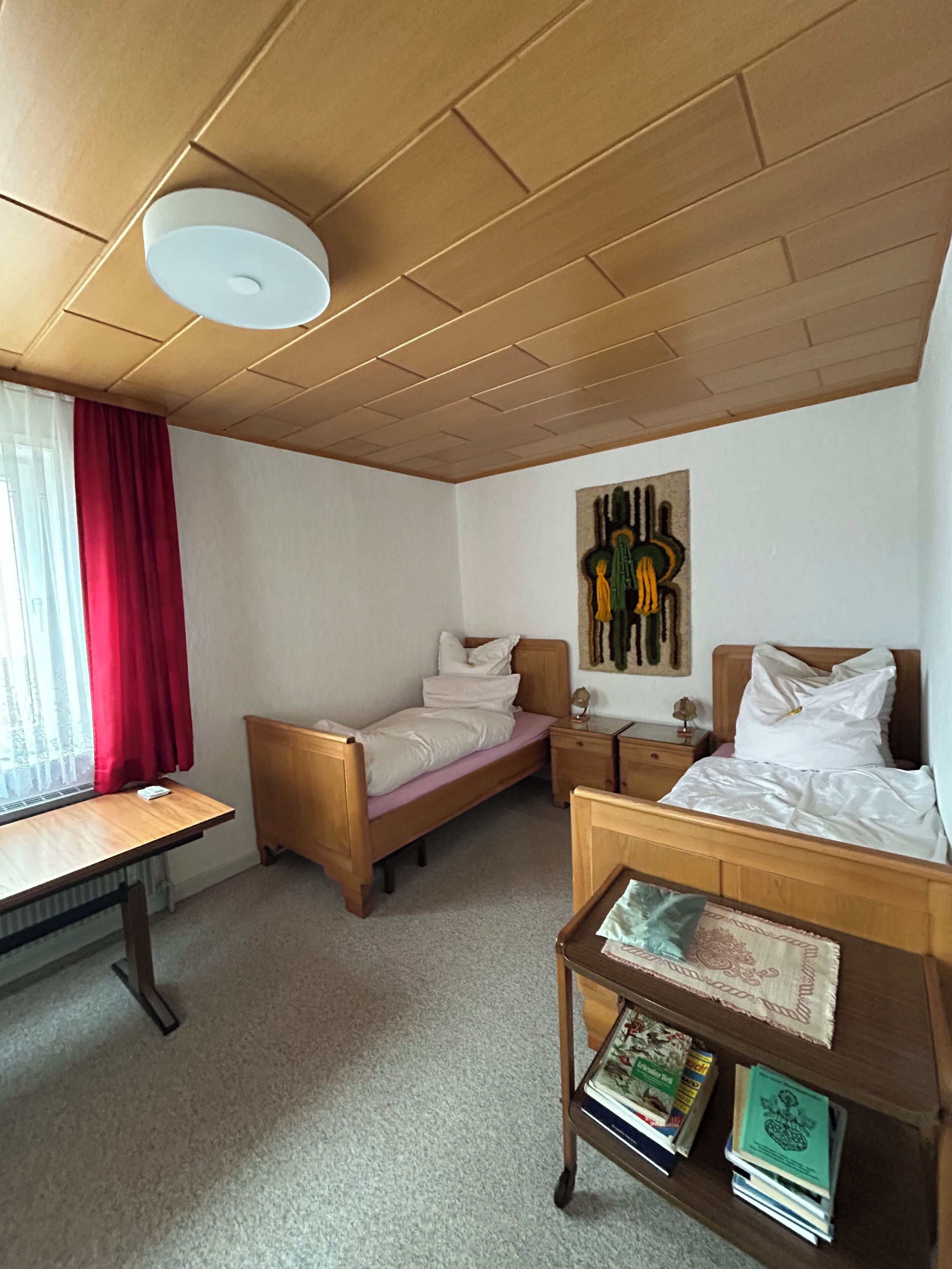 Ein Zimmer mit einem Bett, einem Schreibtisch, einem Sessel, einem Nachttisch und einem Wandbild.
