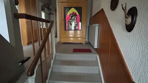 Een trap met houten leuningen, een rode mat onderaan en een aan de muur bevestigde decoratie die op een konijn lijkt.