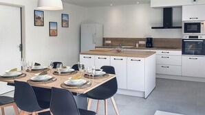 Una cucina moderna con mobili bianchi, un'isola centrale e una zona pranzo con tavolo apparecchiato per quattro persone.
