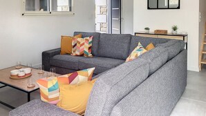 Un soggiorno con un divano grigio, cuscini colorati, un tavolino con bicchieri e un mobile contenitore con piante.