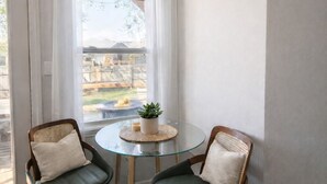 Une pièce avec deux chaises, une table ronde en verre, un luminaire suspendu et une fenêtre avec des rideaux.