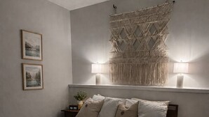 Une chambre à coucher comprenant un lit, une table de chevet, une décoration murale en macramé et deux lampes fixées au mur.