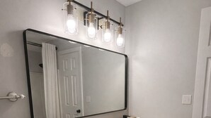 Une salle de bain avec un grand miroir, un lavabo, des placards, une serviette, une plante en pot et un luminaire.
