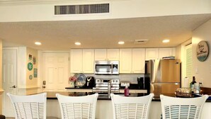 A kitchen with white bar stools, stainless steel appliances, and a clock on the wall.