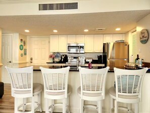 A kitchen with white bar stools, stainless steel appliances, and a clock on the wall. - The Getaway (Myrtle Beach)