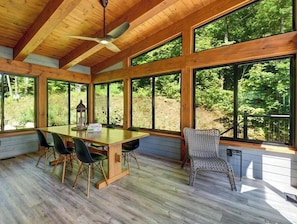 A wooden interior with a table and chairs, large windows, and a ceiling fan. - Serene 6-bedroom Retreat in Tory Hill With Lake Views (North Kawartha)