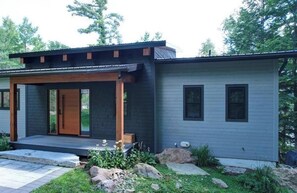 A modern two-story house with a covered porch, a front door, and a small garden area. - Serene 6-bedroom Retreat in Tory Hill With Lake Views (North Kawartha)